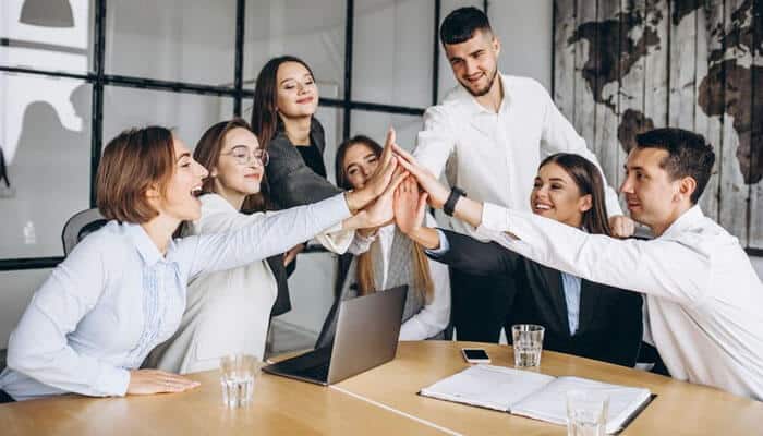 Lifestyle entrepreneur leading a team of young professionals in a modern office, celebrating success with a group high five.