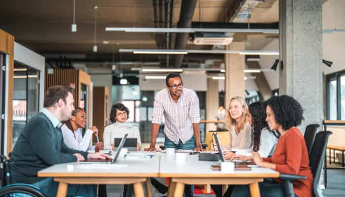 Group of diverse professionals collaborating in a modern office, working together on laptops during a team meeting, fostering creativity and teamwork in a business setting