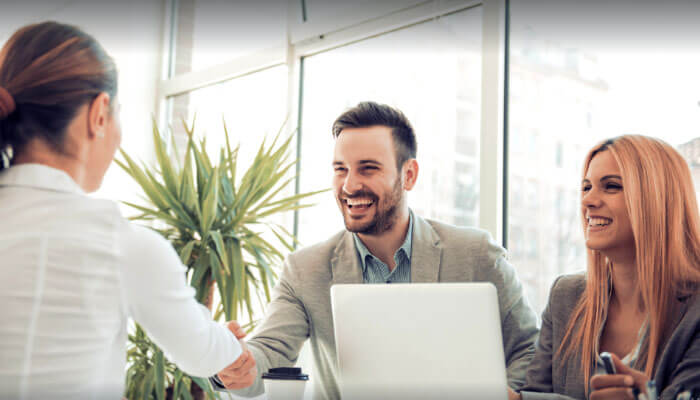 The image shows a job interview scene where a candidate with limited work experience is shaking hands with two interviewers in a professional office setting