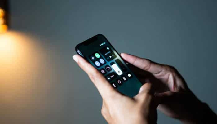 Person navigating Control Center settings to turn off flashlight on iPhone in a dimly lit room