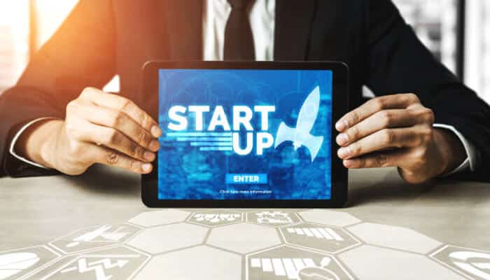 Professional holding a tablet displaying START UP graphic, symbolizing the process of launching your own startup business