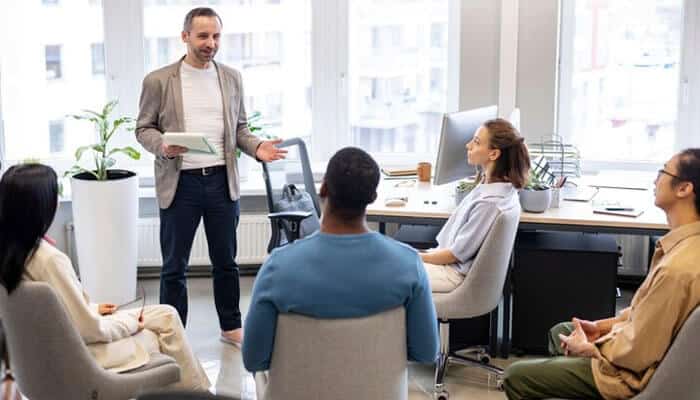 A business coach mentoring a team on how to become a successful entrepreneur in a modern office setting. The group listens attentively in a collaborative space.