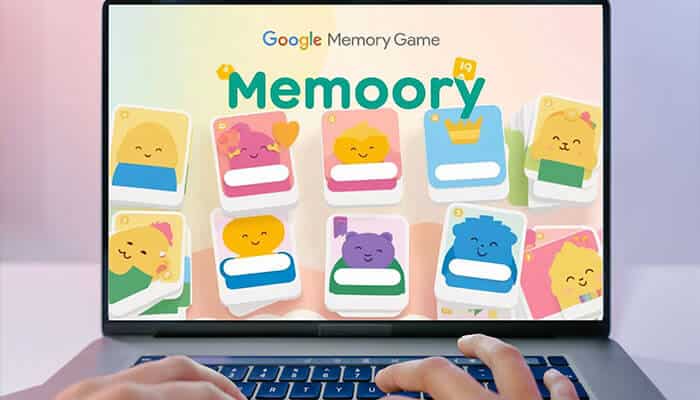 Hands playing the Google memory game on a laptop screen with colorful cartoon cards displayed.