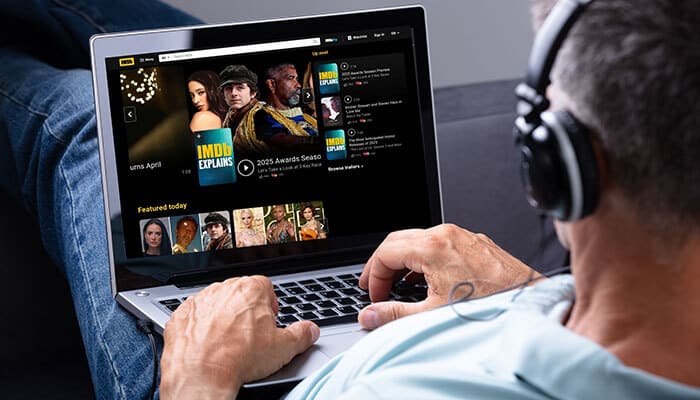 A man wearing headphones using a laptop to browse movies, illustrating how to find a movie by describing it through online platforms