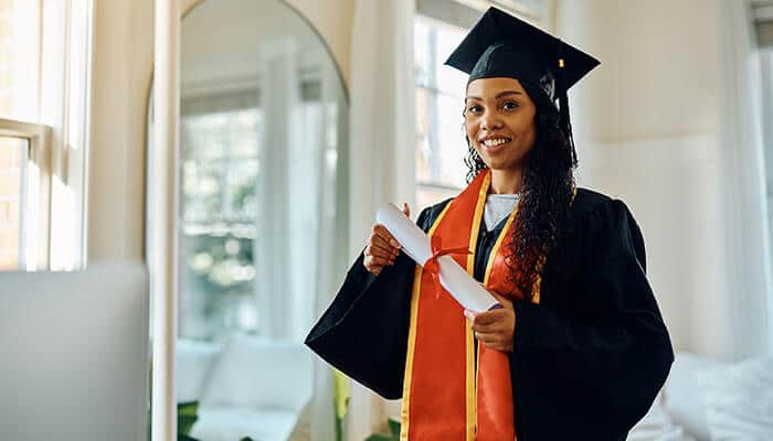 A smiling graduate in cap and gown holding a diploma, celebrating completion of an Online Special Education Masters Program