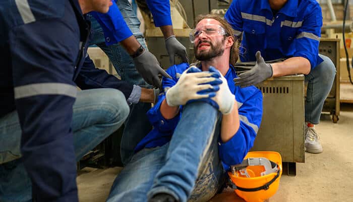 Factory worker in protective gear holding injured leg after workplace accident, highlighting common reasons workers’ compensation claims denied