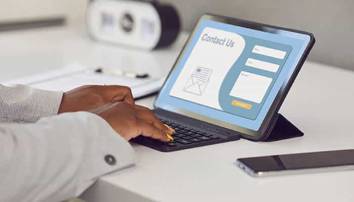 Person typing on a tablet displaying a contact us form, illustrating the importance of custom email design for brand communication and user engagement.
