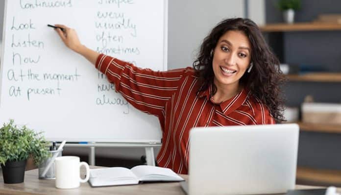 Smiling teacher using a laptop and whiteboard for an online lesson, demonstrating how tech tools in remote teaching enhance interactive learning.