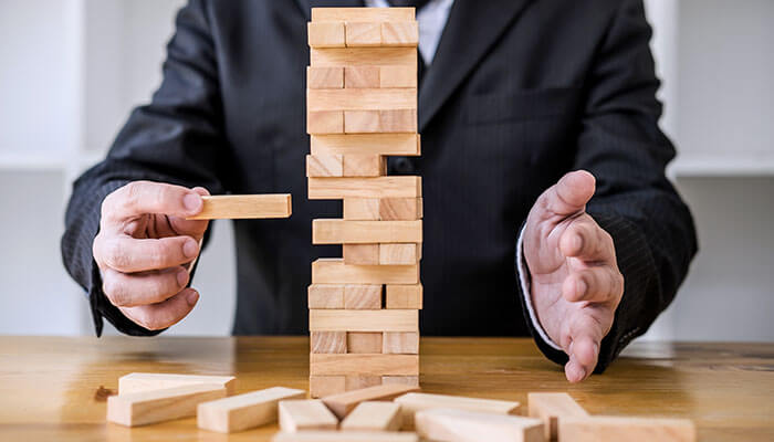 Businessman balancing wooden blocks like a tower game, symbolizing startup scaling priorities, risk management, and stability in growth