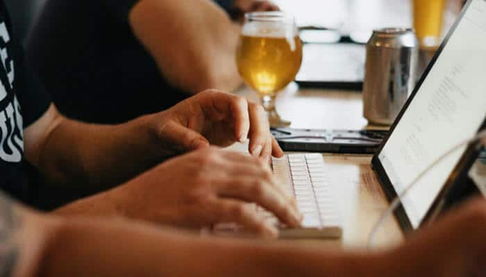 Hands typing on a laptop, working with an opportunity management tool, surrounded by colleagues in a casual workspace.