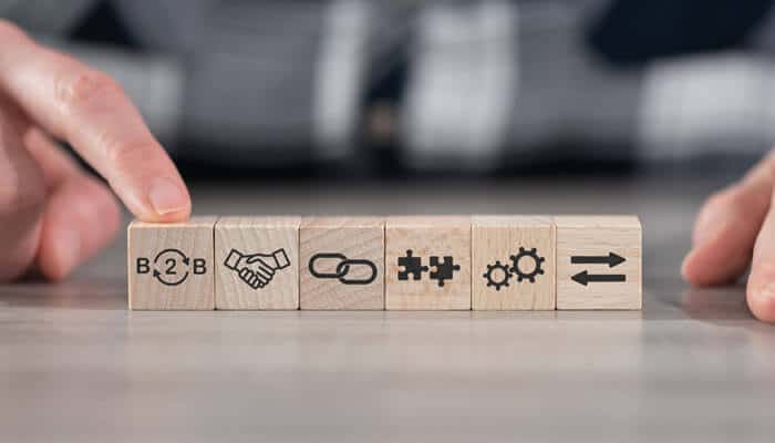 A close-up of wooden blocks displaying icons for B2B, partnership, connection, collaboration, and process efficiency, symbolizing B2B sales success and customer journey optimization.