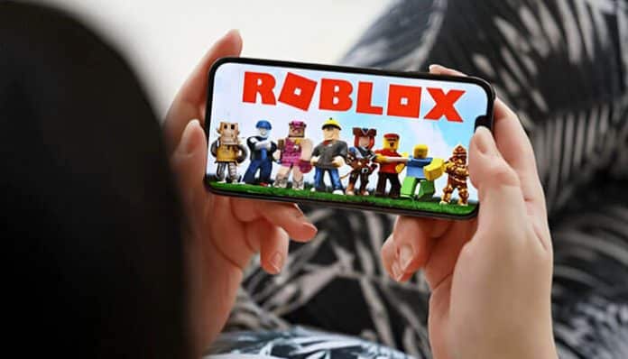 A person holding a smartphone playing Roblox, often used when searching who made Roblox and how the game was created.