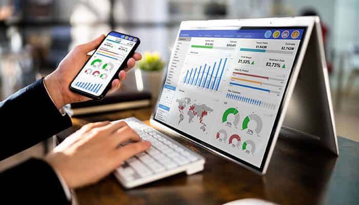 A professional reviewing analytics dashboards on a laptop and smartphone, illustrating the digital tools offered by leading board management software providers.