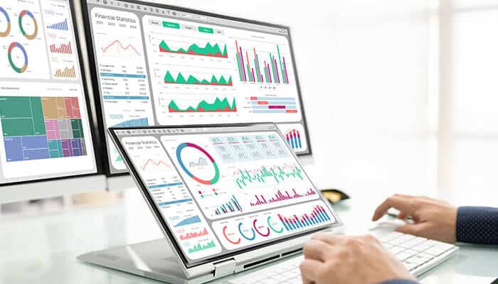 Healthcare professional analyzing data on multiple screens, visualizing performance metrics and analytics, showcasing the impact of EAM in the healthcare industry