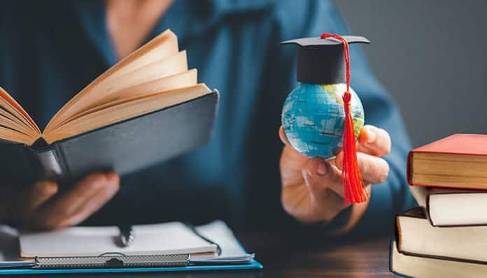 Person reading a book while holding a globe with a graduation cap, symbolizing global learning disparities and highlighting differences in economic education by state