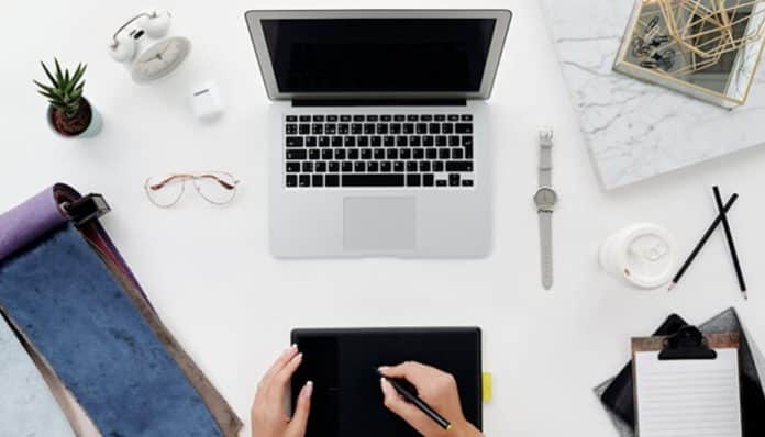 Person working at a desk with a laptop and notebook illustrating automating performance reviews